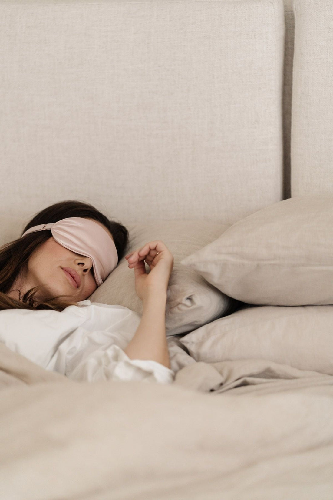 Jeune femme allongé sur un lit de haute qualité beige et un masque sur les yeux rose 